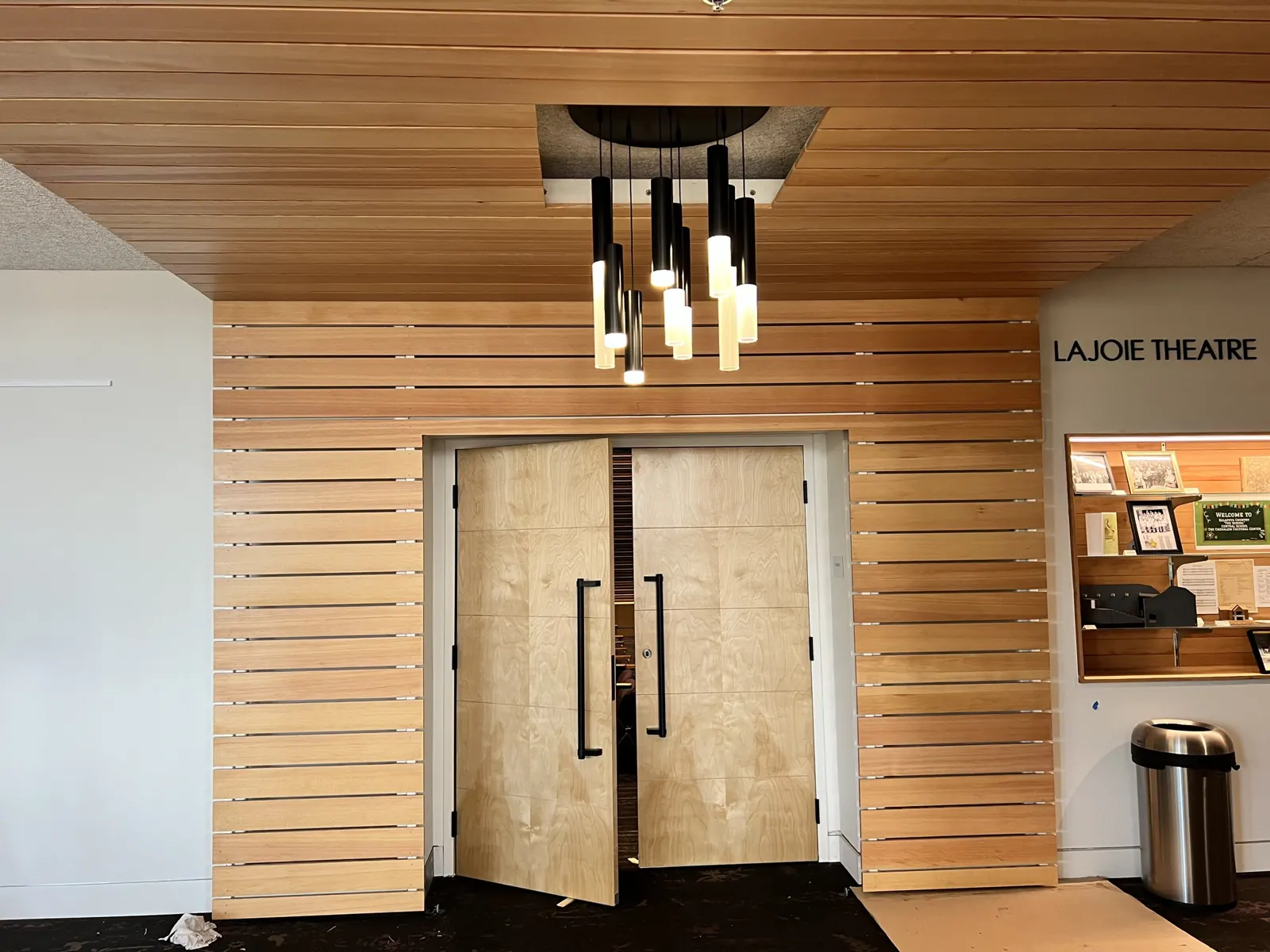 Wood slat ceiling and walls wrapping a pair of doors, with a pendant light